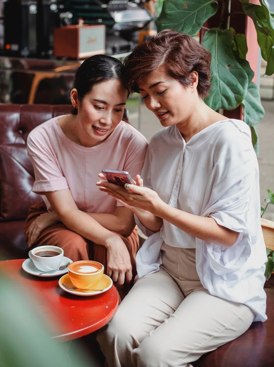 Two friends looking at a phone together at a cafe.