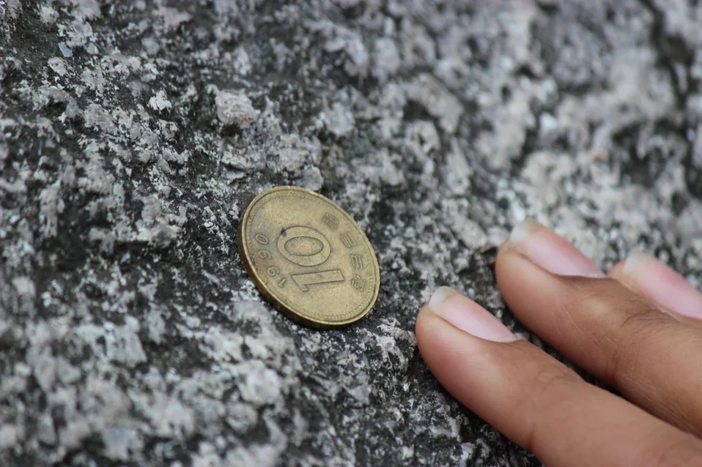 A Korean won coin on a stone surface beside a hand.