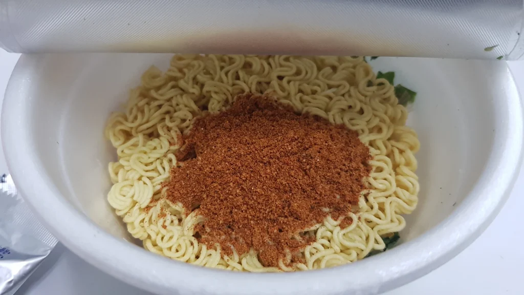 Powdered soup seasoning added to the dry noodles in an open cup.