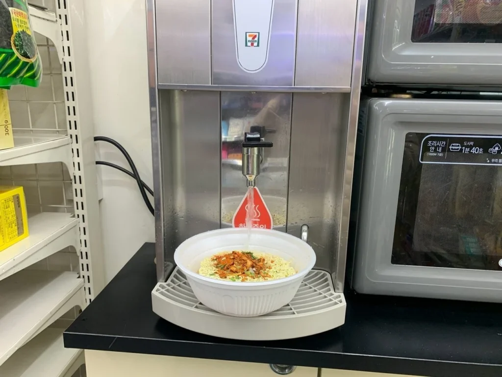 A Wang Ttukkeong noodle cup resting under a hot-water dispenser in a Korean 7-Eleven.