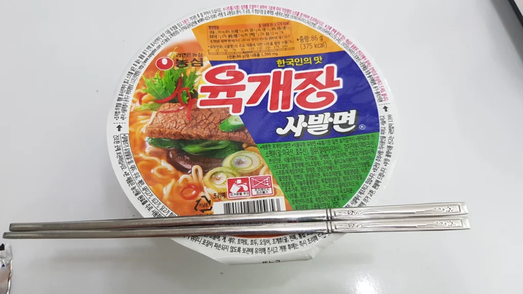 A noodle cup with its lid closed and chopsticks resting across it.