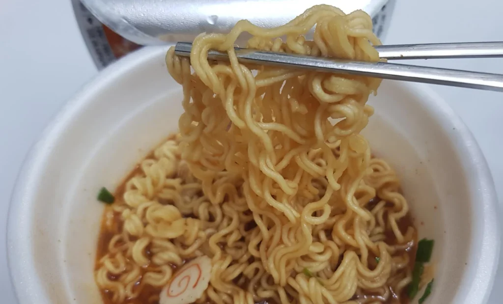 Cooked noodles lifted from a Yukgaejang cup with chopsticks.