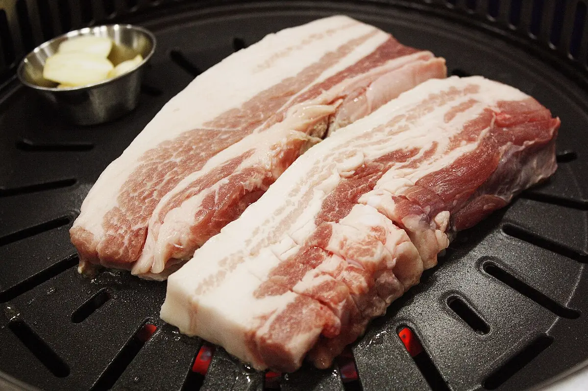 Raw pork belly slices with visible layers of fat on a grill.