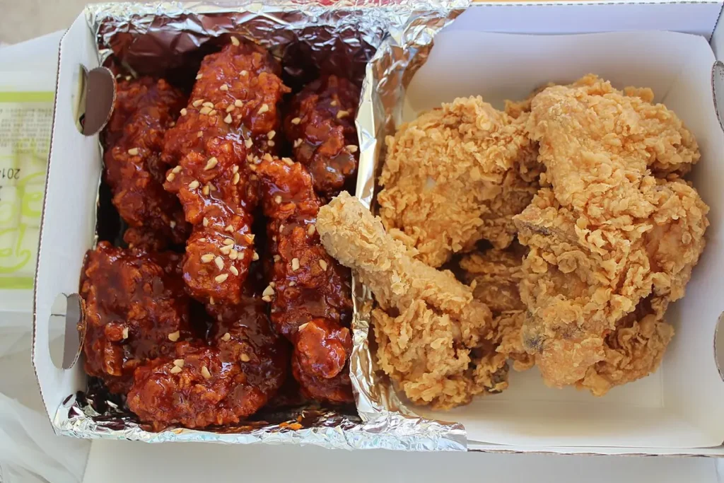 A divided takeaway box holding seasoned and plain fried chicken.