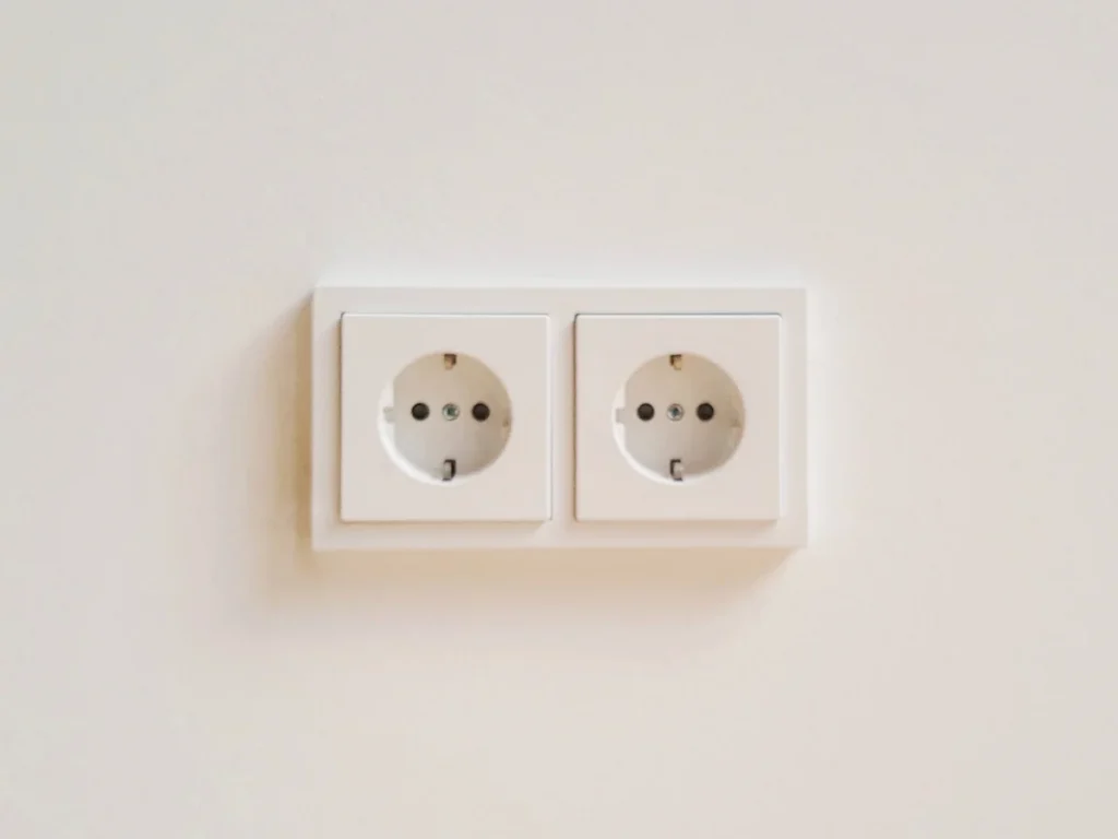 A white double wall socket in Korea with two round holes and metal grounding clips in each recess.