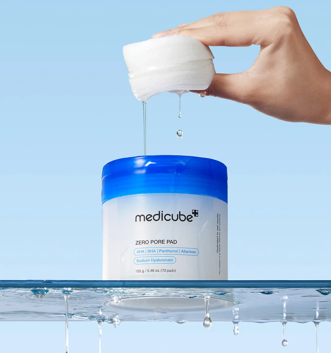 A hand squeezing a stack of medicube Zero Pore Pads above the jar with toner dripping