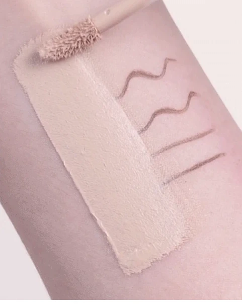 A concealer wand spreading beige product across marked skin in the brand demonstration.