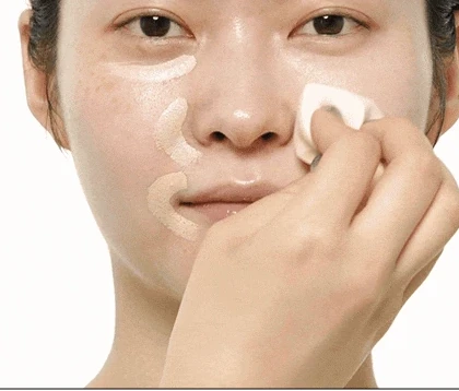A sponge pressing and blending concealer over the cheek.